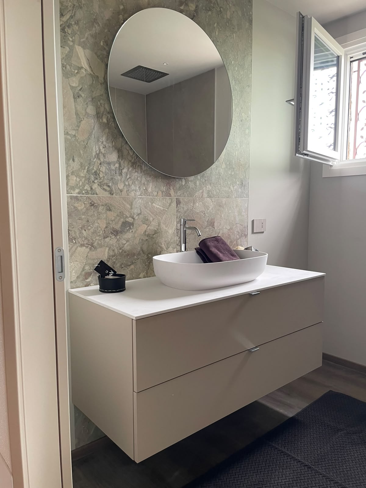 Badezimmer mit Waschtisch, rundem Spiegel und Natursteinoptik